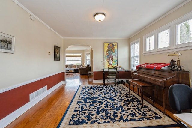 home office with arched walkways, a wealth of natural light, wood finished floors, and visible vents