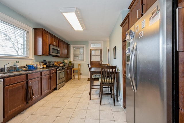 kitchen featuring light tile patterned floors, stainless steel appliances, a sink, baseboards, and dark countertops