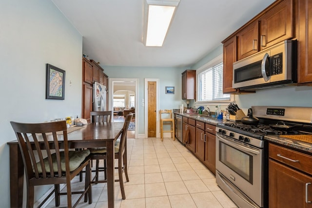 kitchen featuring arched walkways, light tile patterned floors, stainless steel appliances, a barn door, and a sink