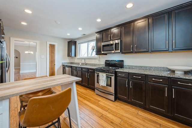 kitchen with light wood finished floors, a breakfast bar area, appliances with stainless steel finishes, a sink, and recessed lighting