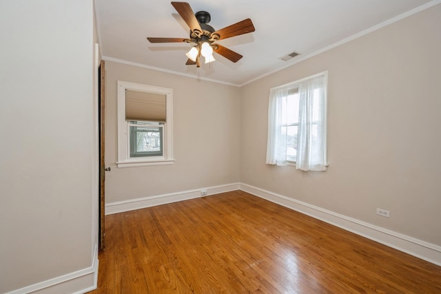 empty room featuring ornamental molding, visible vents, baseboards, and wood finished floors