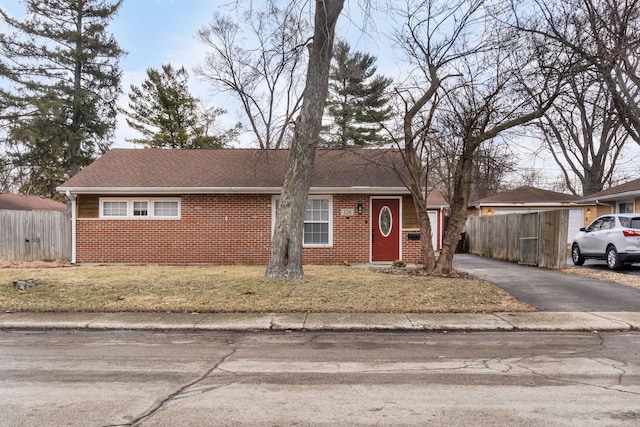 ranch-style house featuring brick siding, fence, driveway, roof with shingles, and a front yard