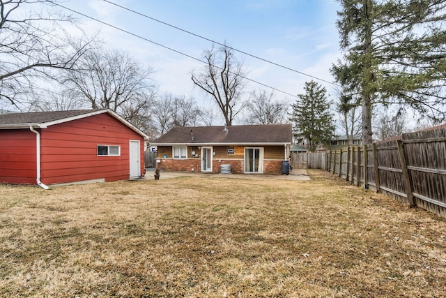 back of house featuring an outbuilding, a fenced backyard, a lawn, and brick siding