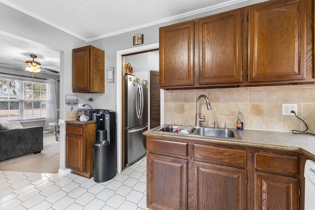 kitchen with brown cabinetry, ceiling fan, freestanding refrigerator, a sink, and backsplash