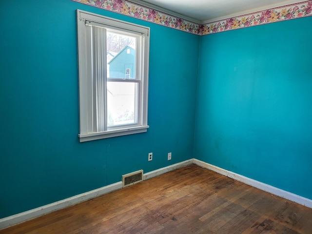 empty room with a healthy amount of sunlight, wood-type flooring, visible vents, and baseboards