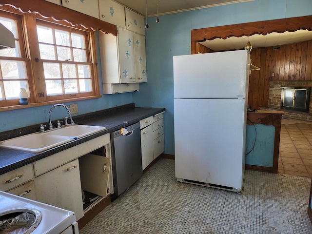 kitchen with a sink, dark countertops, stainless steel dishwasher, and freestanding refrigerator