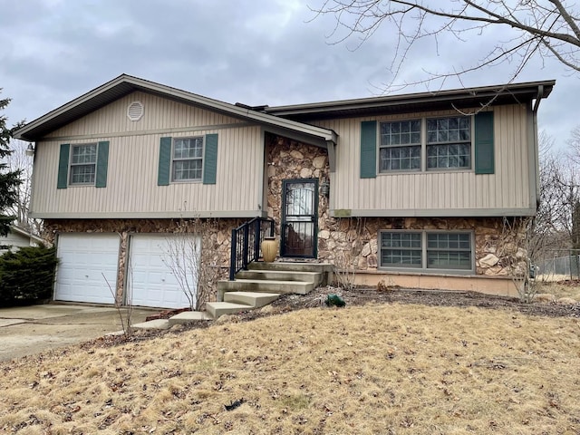 bi-level home featuring an attached garage, stone siding, and concrete driveway