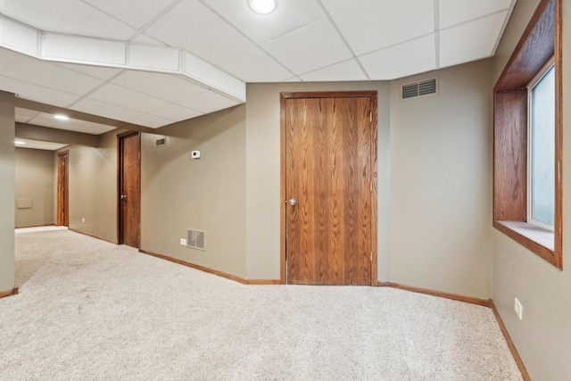 finished below grade area with carpet floors, baseboards, visible vents, and a drop ceiling