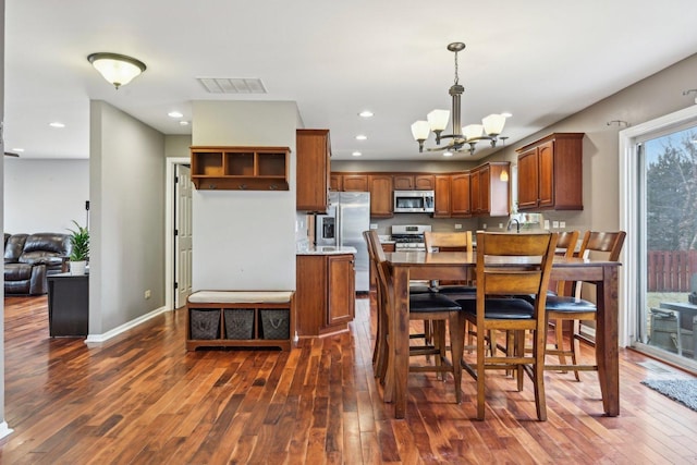 kitchen with dark wood-style floors, brown cabinets, decorative light fixtures, visible vents, and appliances with stainless steel finishes