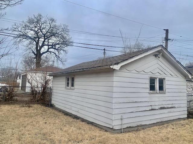 view of side of home with a shingled roof, a lawn, an outdoor structure, and fence