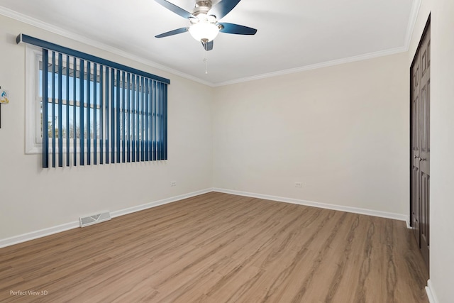 empty room featuring crown molding, visible vents, a ceiling fan, wood finished floors, and baseboards