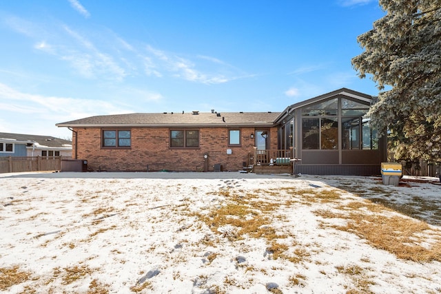 snow covered back of property with brick siding and fence