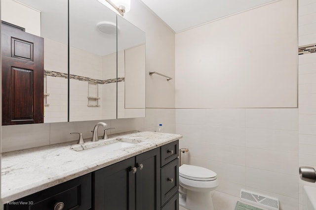 bathroom with toilet, vanity, visible vents, and tile walls