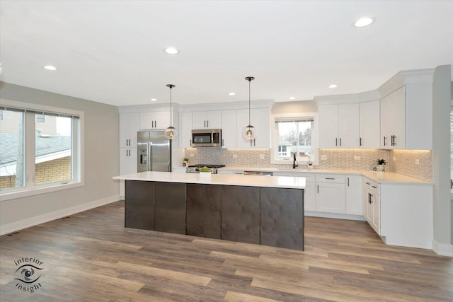 kitchen with a center island, hanging light fixtures, stainless steel appliances, light countertops, and white cabinetry