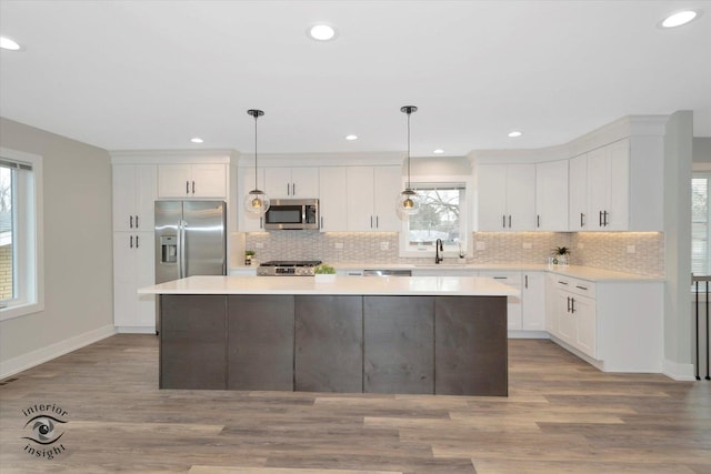 kitchen with stainless steel appliances, a kitchen island, white cabinets, hanging light fixtures, and light countertops