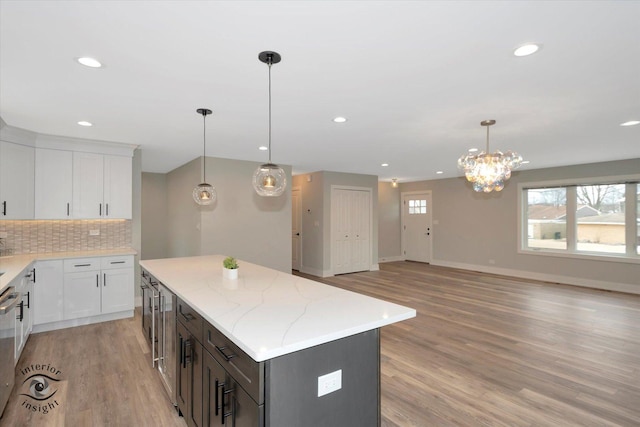 kitchen with light stone counters, a kitchen island, white cabinets, tasteful backsplash, and pendant lighting