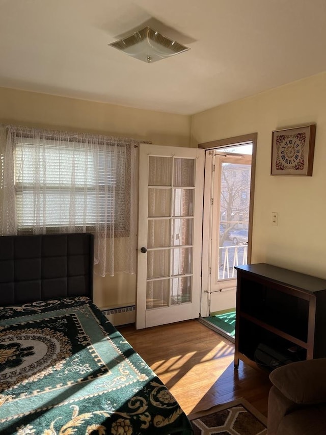 bedroom with a baseboard radiator, dark wood finished floors, visible vents, and access to exterior