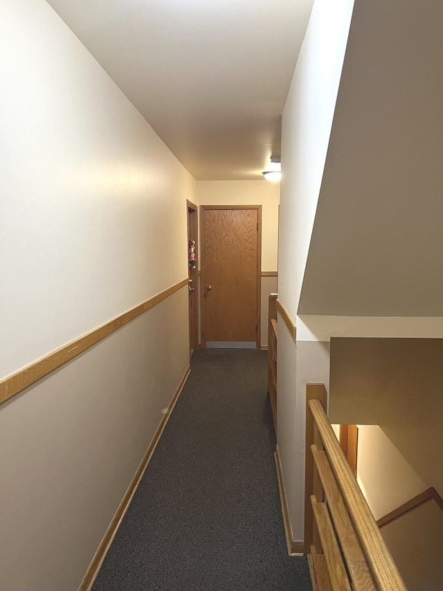 corridor with baseboards, dark colored carpet, and an upstairs landing