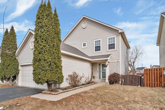 traditional-style house featuring driveway, roof with shingles, an attached garage, and fence