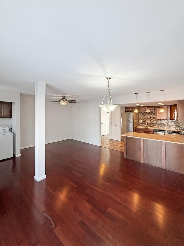 unfurnished living room with dark wood-type flooring, washer / clothes dryer, ceiling fan, and baseboards