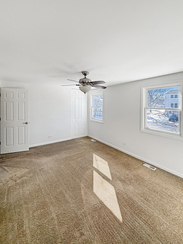 carpeted empty room featuring a ceiling fan, visible vents, and baseboards