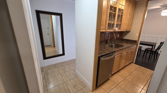 kitchen featuring brown cabinets, stainless steel dishwasher, glass insert cabinets, a sink, and dark stone counters