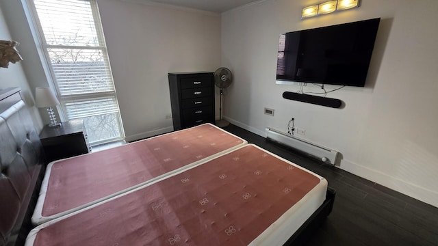 bedroom featuring dark wood-style flooring, baseboards, baseboard heating, and crown molding