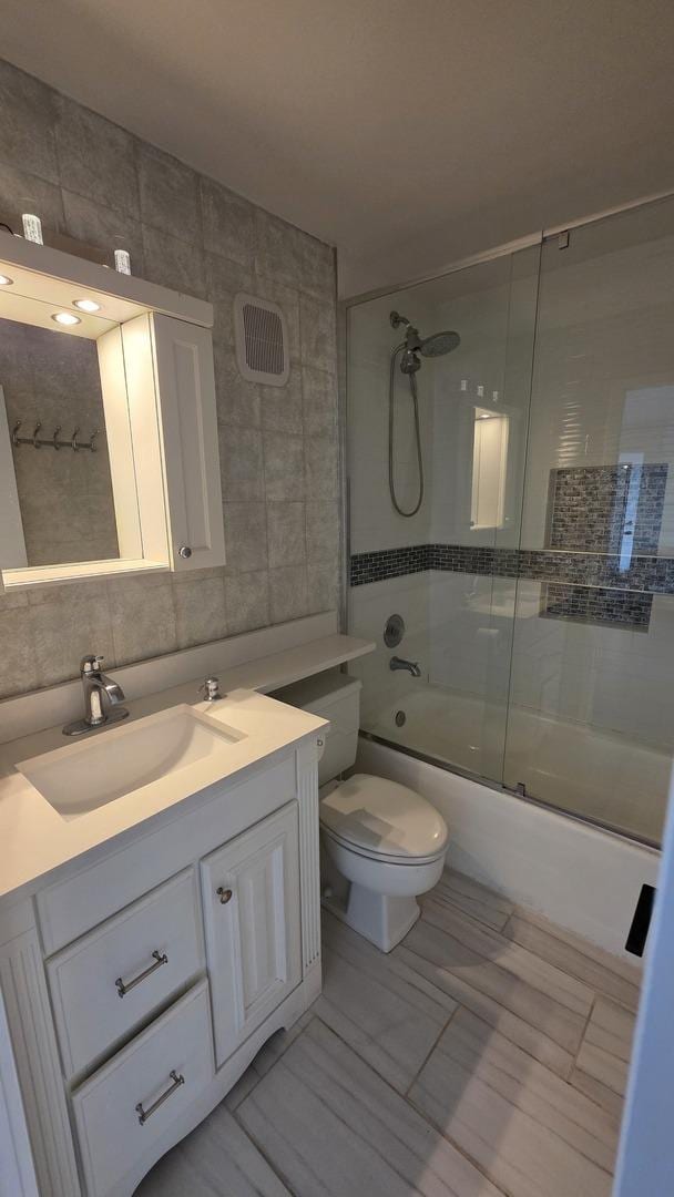 full bathroom featuring toilet, shower / bath combination with glass door, vanity, tile walls, and tasteful backsplash