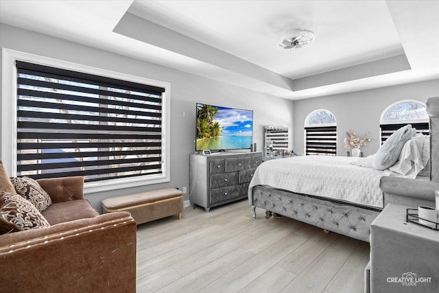 bedroom with light wood-type flooring and a raised ceiling