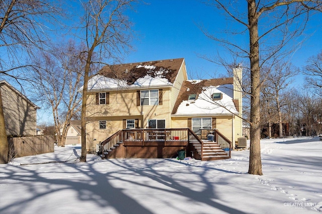 snow covered back of property with a chimney, a wooden deck, and central air condition unit