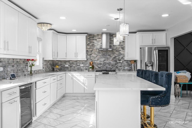 kitchen with wine cooler, a kitchen island, decorative light fixtures, wall chimney range hood, and white cabinetry