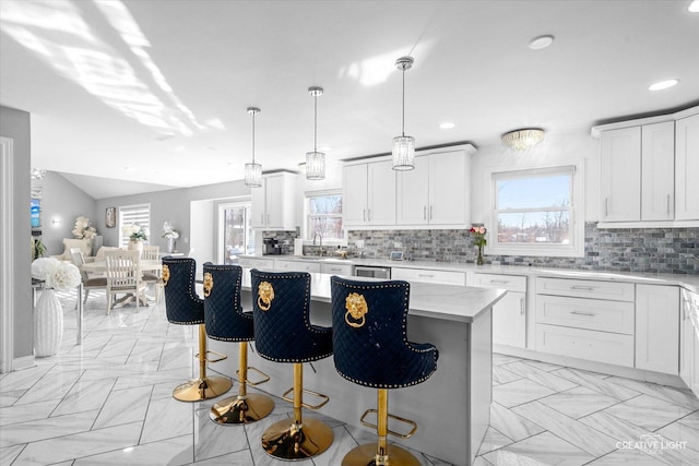 kitchen featuring a center island, white cabinets, hanging light fixtures, a wealth of natural light, and light stone countertops