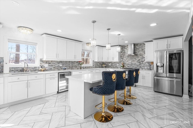 kitchen featuring beverage cooler, stainless steel fridge with ice dispenser, a center island, light countertops, and wall chimney range hood