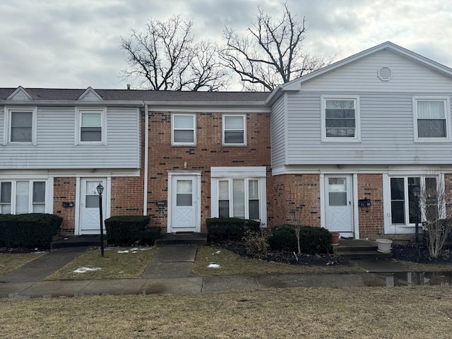 townhome / multi-family property with entry steps, brick siding, and a front yard