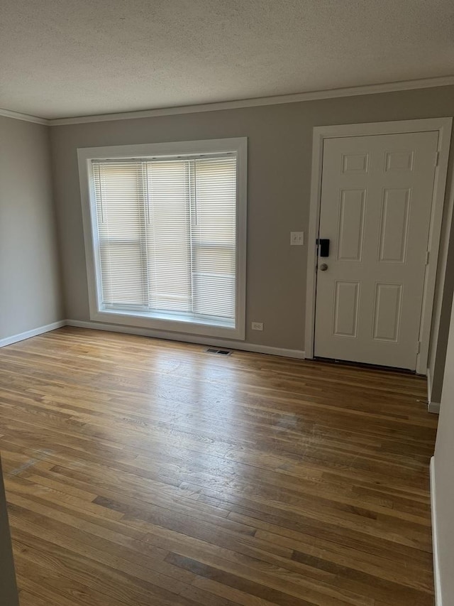 entryway featuring baseboards, visible vents, wood finished floors, crown molding, and a textured ceiling