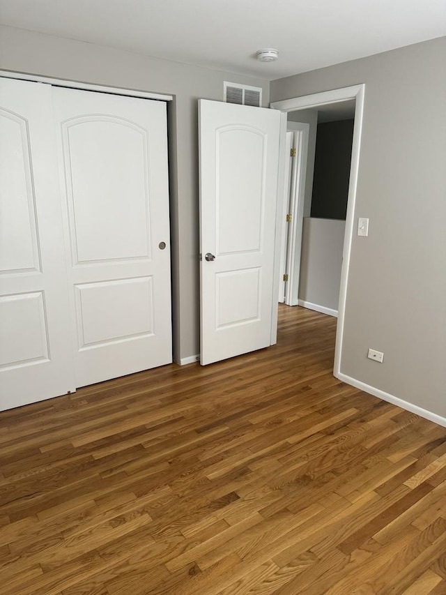 unfurnished bedroom with a closet, dark wood-style flooring, visible vents, and baseboards