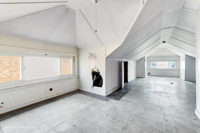 additional living space with baseboards, vaulted ceiling, and light floors