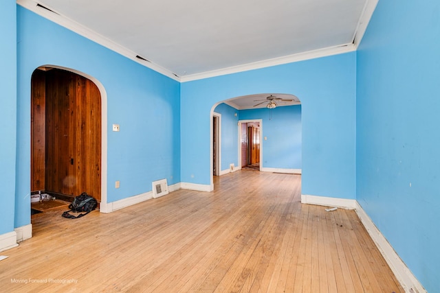 spare room featuring baseboards, arched walkways, hardwood / wood-style floors, and ornamental molding