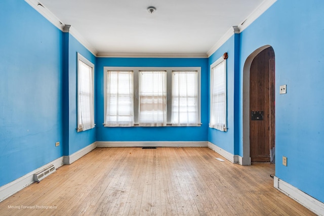 empty room featuring light wood finished floors, visible vents, arched walkways, baseboards, and ornamental molding