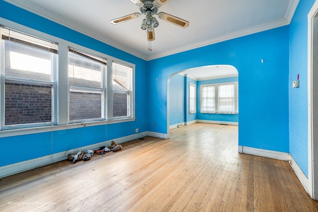 empty room featuring arched walkways, baseboards, crown molding, and light wood finished floors