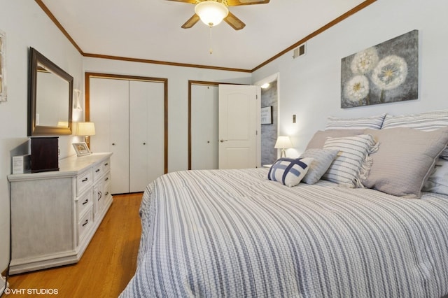 bedroom with ornamental molding, light wood-style floors, visible vents, and multiple closets