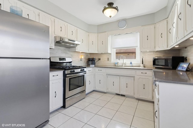 kitchen featuring tasteful backsplash, under cabinet range hood, appliances with stainless steel finishes, light tile patterned flooring, and a sink