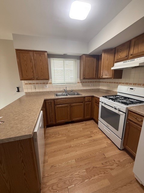 kitchen with white appliances, decorative backsplash, a peninsula, light wood-type flooring, and under cabinet range hood