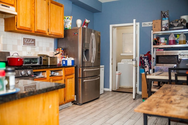 kitchen featuring light wood finished floors, decorative backsplash, brown cabinetry, washer / dryer, and under cabinet range hood