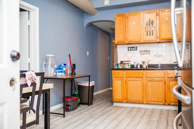 kitchen featuring arched walkways, light wood finished floors, backsplash, and a sink