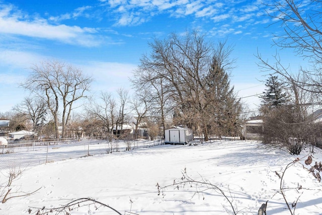 yard layered in snow featuring an outbuilding, fence, and a storage shed