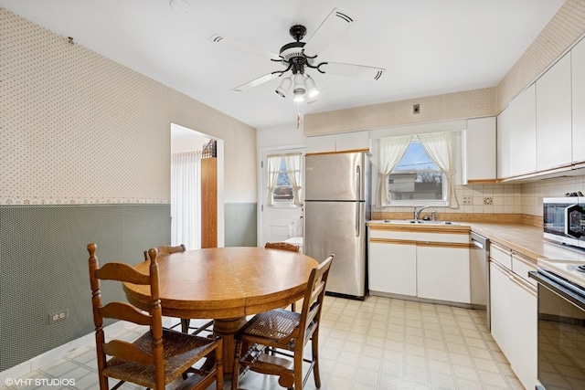 kitchen featuring stainless steel appliances, a sink, light countertops, light floors, and wallpapered walls