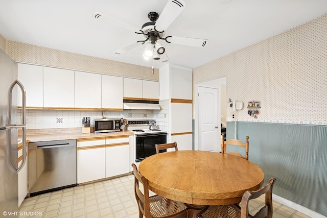 kitchen featuring under cabinet range hood, stainless steel appliances, white cabinetry, light countertops, and wallpapered walls