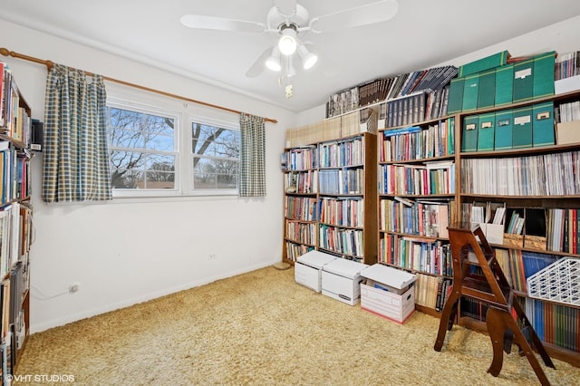 sitting room with wall of books, carpet, and a ceiling fan