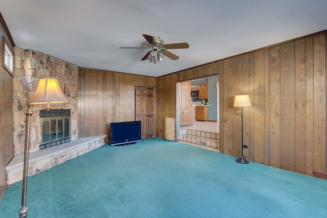 unfurnished living room featuring wooden walls, carpet, a fireplace, and a ceiling fan